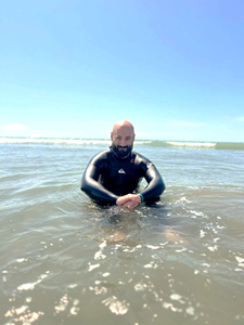 Jonathan Stone photograph of Jonathan Stone in water at a beach - he is in a wet suit and smiling