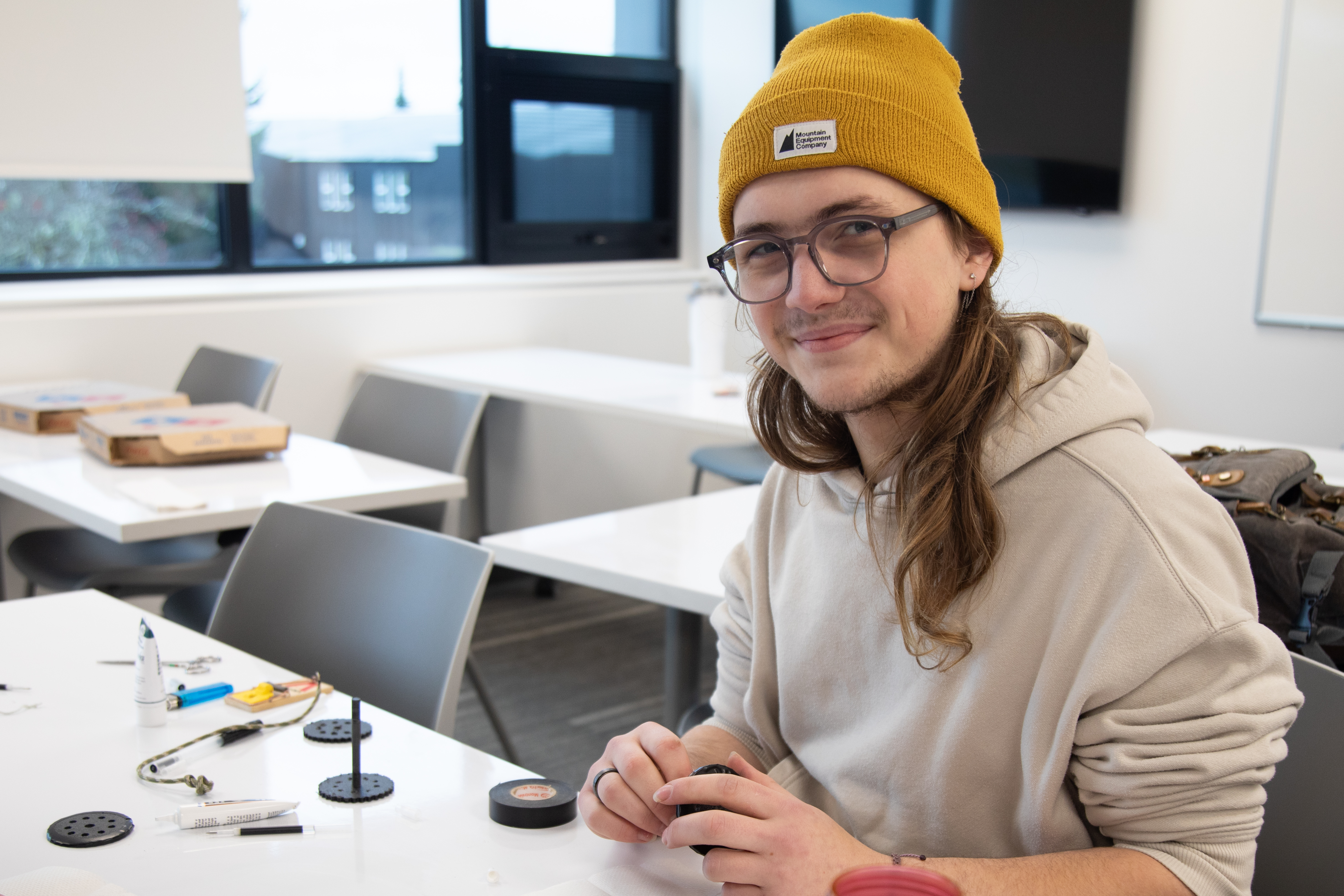 A student assembles a hands-on project while seated at a table with tools and components in front of them.